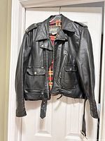 Full view of black leather motorcycle jacket on hanger showing overall style and condition