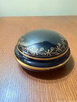 Closed black porcelain trinket box showing gold floral motif and gold rim