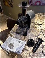 Juicer assembled with containers, auger, end cap and manual on countertop
