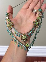 Necklace draped on hand showing floral stations, bead and leaf dangles