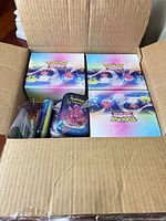 Open shipping carton showing four sealed Pokémon TCG display boxes and visible tins