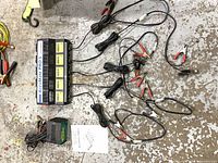 AccuMate PRO 5 charger with five banks, attached leads and clamps, Battery Tender Plus maintainer visible