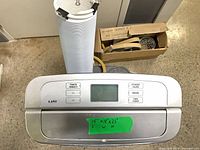 Top control panel of LG LP1311BXR with display, buttons and taped dimensions plus exhaust hose and boxed window kit in background