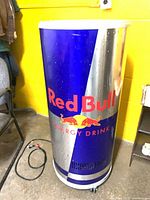 Full view of cylindrical Red Bull refrigerator on casters with power cord