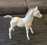Left side profile of white foal figurine showing body, legs, tail