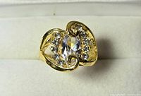 Ring front view showing gold-tone swirl design with center oval clear stone and surrounding round stones