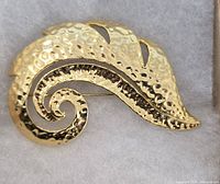front view of hammered gold-tone leaf brooch showing design and texture