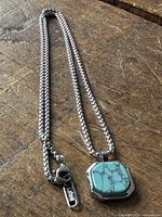 Full view of necklace showing box chain, pendant, and clasp with branded tag