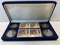 Open presentation case showing four coins and four stamps in recessed velvet tray