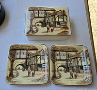 Overall view of trinket box with lid on and two matching dishes showing village scene