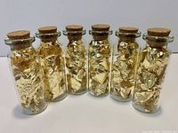 Six small glass bottles with corks, filled with gold leaf flakes, lined up