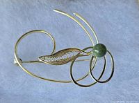 Overview of gold-tone brooch showing filigree leaf, loops, green bead, and clasp