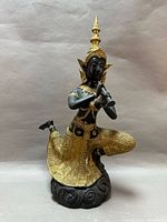 Front view of black and gold Thai deity statue playing flute