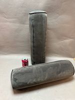 Two gray cylindrical cushions standing and lying beside soda can for scale