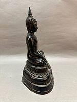 Right side view of dark metal seated Buddha on tiered base