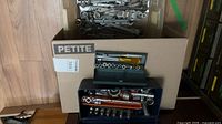 Overall view: cardboard box labeled PETITE filled with loose wrenches; dark blue and green socket sets placed in front