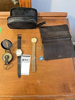 All items laid out: compass, two watches, wallet, pin, buckle, black pouch