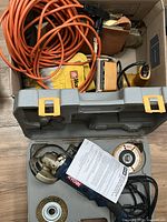 Box containing extension cord, sander, gloves, sandpaper, Ryobi case open with grinder and discs