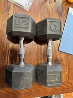 Pair of 25 lb rubber hex dumbbells on wooden surface, showing 25 marking and flame logo