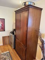 Full view of tall wooden armoire next to wall, top crown and side panels visible