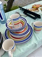 Multicolour striped mugs stacked with matching plates and bowls on table