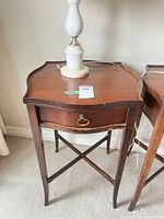 First table front view showing serpentine top, drawer with brass pull, tapered legs, lamp excluded