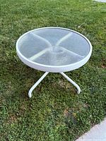 Round white aluminum patio table with glass top on grass