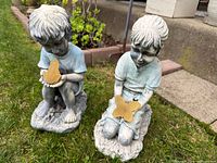 Two child garden statues on grass, each holding yellow butterfly light