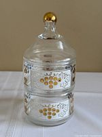 Full view of stacked jar showing grape and vine panels and gold finial