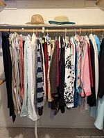 Closet rod filled with hanging women’s clothing; two straw sun hats on shelf above