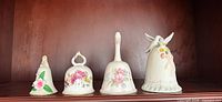 Four floral porcelain bells lined on shelf showing fronts and decorative details