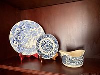 Large Gay Day Blue plate, small floral plate, Currier and Ives gravy boat on shelf