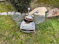 Front view of metal bee sculpture showing wings, antennae, mouth and body on grass