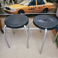 two black plastic round stools with silver legs on carpet