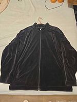 Front view of black velour Adidas track jacket laid flat