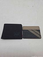Front view of black Herschel bi-fold wallet and tan/black striped card sleeve