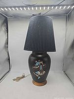 Full view of black ceramic lamp with wooden base and pleated black shade