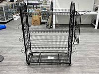 front view of black metal wire shelving unit showing four shelves, side baskets, and casters