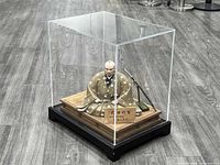 Overall view of samurai figure inside clear acrylic case on black base showing figure, sword, plaque and platform