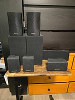 Group of seven black wired speakers; two small Onkyo, two larger Onkyo, two Panasonic cubes, one horizontal center