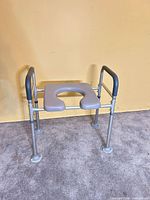 Front angled view of aluminum commode frame with gray seat and padded armrests