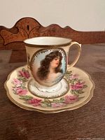 Cup on saucer showing portrait, floral decoration, gold trim