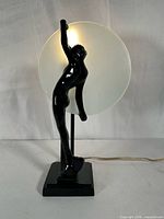 Front view of glossy black female figure lamp with frosted glass disc illuminated