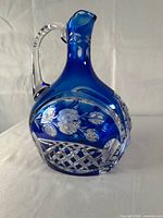 Side view of cobalt blue cut glass pitcher showing floral and lattice cuts, applied handle visible