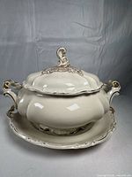 Front view of cream and gold porcelain covered tureen on underplate