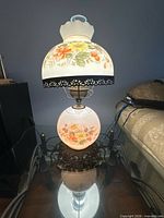Both lamps on glass table illuminated showing floral milk glass shades and globes