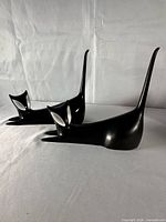 Two elongated black ceramic cat figurines lying side by side, front view showing white eyes