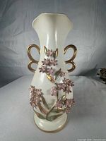 Front view of cream porcelain vase showing pink floral appliqués and gold scroll handles