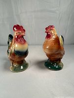 Front three-quarter view of rooster and hen figurines showing glaze colors and overall condition