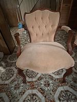 Front view of upholstered French Provincial armchair showing tufted backrest, carved frame and cabriole legs